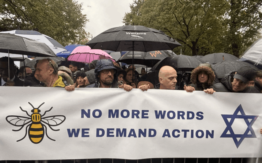 Crowds at the Manchester vigil hold a banner reading “No more words, we demand action” in pouring rain