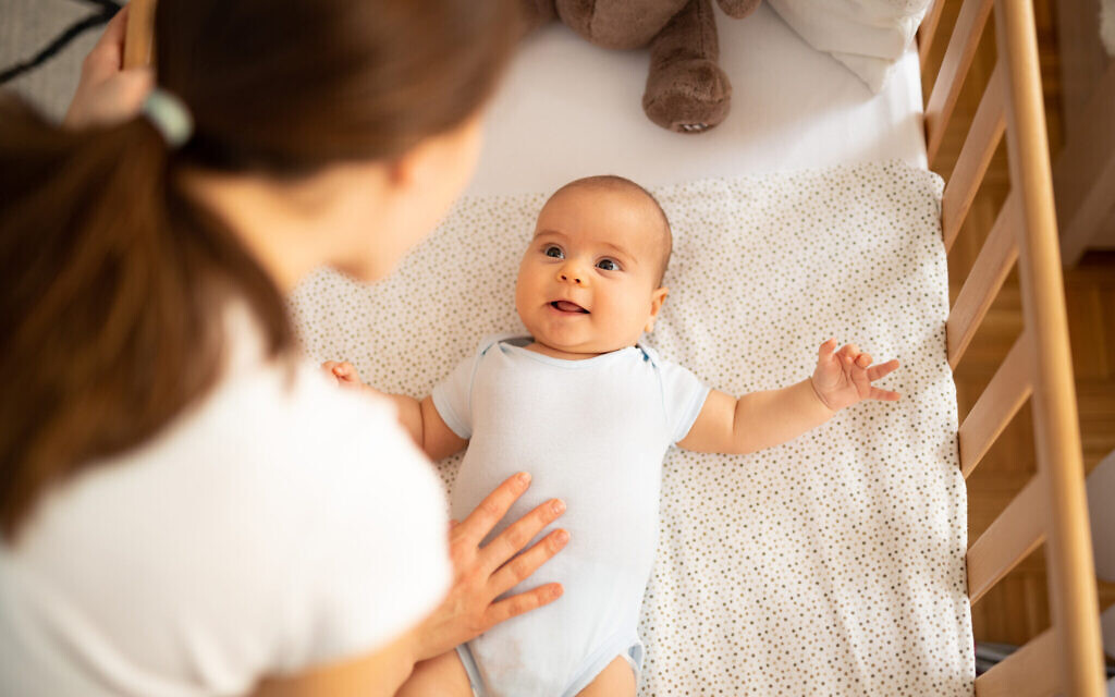 Mother leaning over side of crib and talking to her baby boy. Child looking at mum and smiling