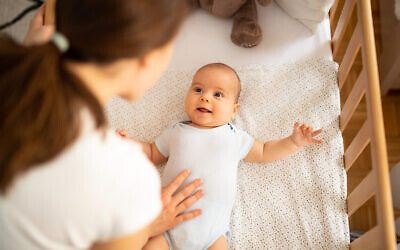 Mother leaning over side of crib and talking to her baby boy. Child looking at mum and smiling