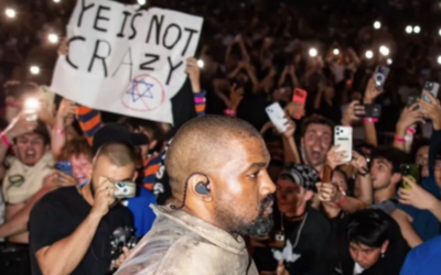 A fan holds a sign reading "YE IS NOT CRAZY" alongside a crossed-out Star of David as Kanye West performs at a concert in Tampa Bay