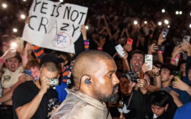 A fan holds a sign reading "YE IS NOT CRAZY" alongside a crossed-out Star of David as Kanye West performs at a concert in Tampa Bay