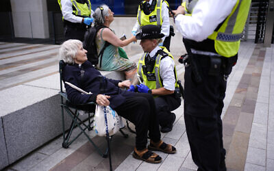A police officer detains Reverend Sue Parfitt who declared her support for Palestine Action outside the headquarters of the Metropolitan Police at New Scotland Yard, central London, to mark one-year of the group being proscribed as a terror organisation.